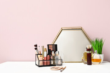 Different cosmetic products, mirror and houseplant on dressing table near pink wall in room