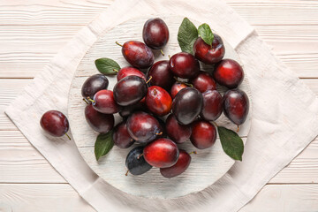 Board with fresh ripe plums and leaves on white wooden background