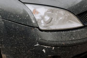 Dirty headlights, cracked bumper, rusty body, gray car surface. Close-up photo.