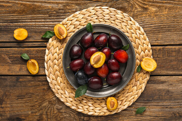 Plate with fresh ripe plums and leaves on wooden background