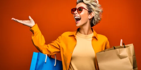 Foto op Canvas Joyful woman with shopping bags pointing away on orange background © Bartek