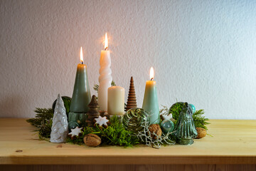 Third Advent, decoration with four different candles, three are lit, some moss, green Christmas...