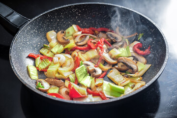 Steaming vegetables are stir-fried in a frying pan with healthy ingredients such as peppers, mushrooms, onions and cabbage, selected focus