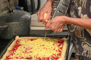woman prepares pizza with cheese, tomatoes and chicken ham, woman rubs cheese 10