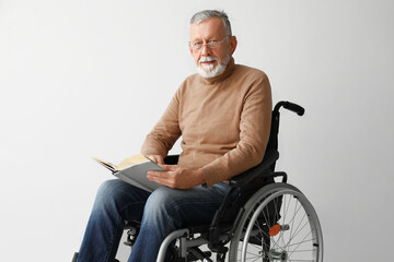 Senior man in wheelchair reading book on light background