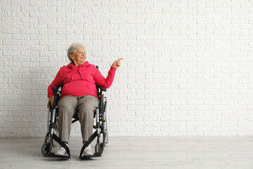 Senior woman in wheelchair pointing at something near white brick wall