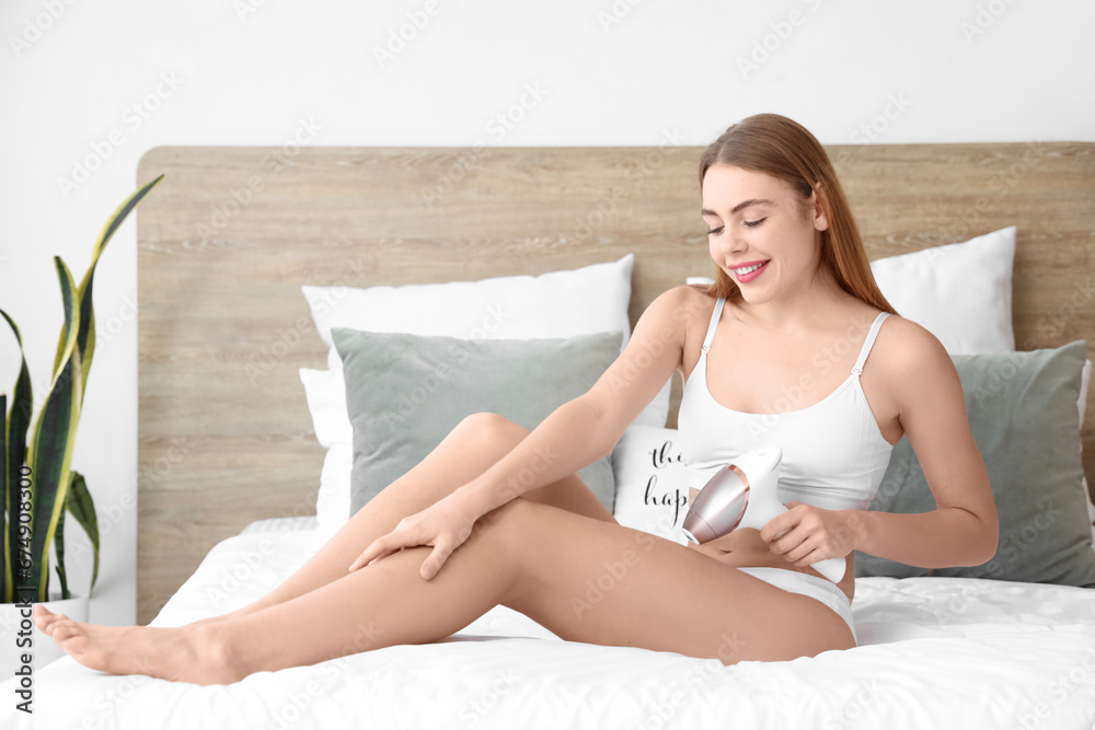 Sticker Young woman epilating her legs with modern photoepilator in bedroom at home