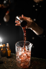 Female hand pours an alcoholic drink from a jigger into a glass with ice