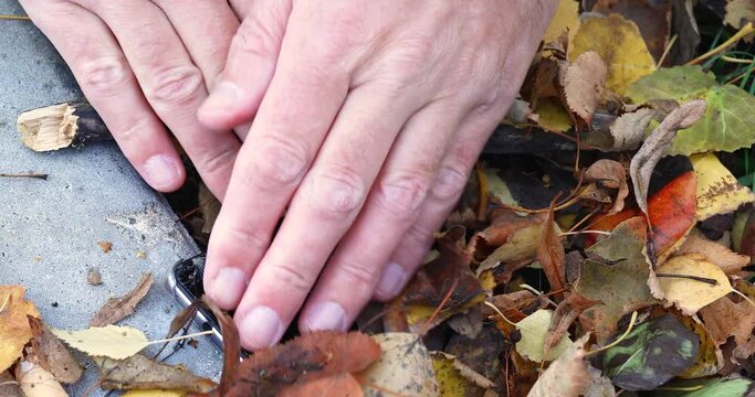 A man finds a smartphone on the street with a broken screen, slightly covered with autumn leaves, and picks it up from the ground