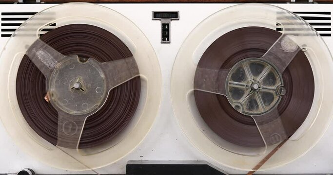 An old reel-to-reel tape recorder plays a melody on magnetic tape, vintage music player close-up