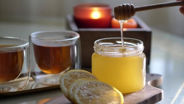 Close up honey flowing from wooden dipper on table with tea and lemon