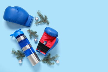 Boxing gloves, sports bottle with Christmas tree branches and balls on blue background