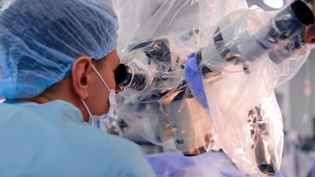 Rear view of a doctor in mask and cap looking into microscope. Neurosurgeons at work. Close up.