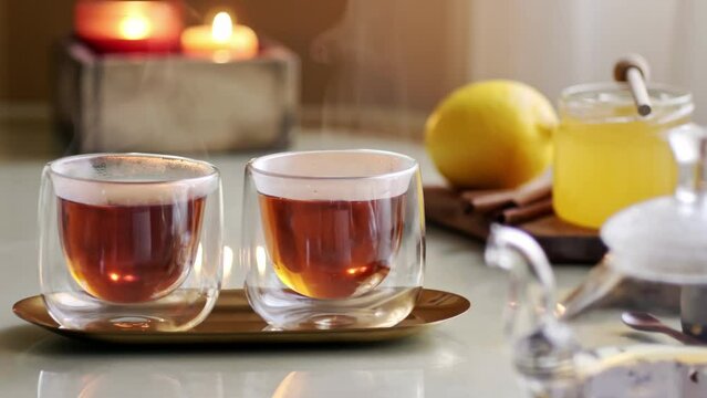 Pair of double glass transparent cups with hot steaming tea on tray 