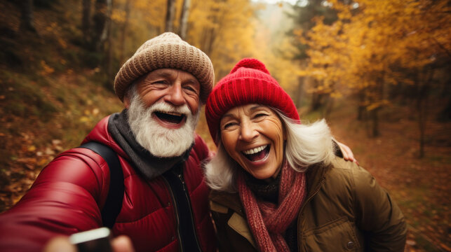 POV portrait of active senior couple looking at camera and smiling while taking selfie photo during hike in autumn forest, copy space
