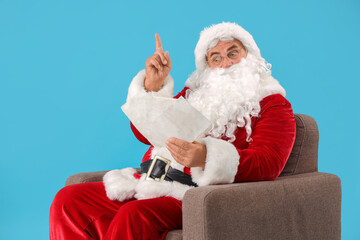 Santa Claus with letters in armchair pointing at something on blue background
