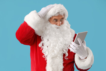 Shocked Santa Claus with tablet computer on blue background