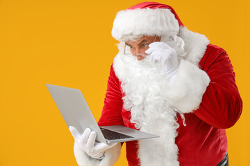 Shocked Santa Claus with laptop on yellow background