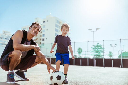 Father teaching son how to play football. Little boy preparing to kick soccer ball in public park