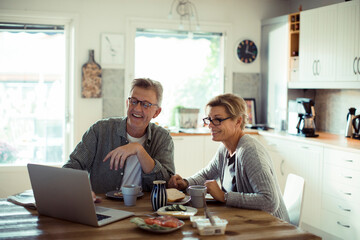 Middle aged couple using laptop during morning breakfast in kitchen