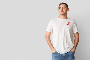 Fototapeta premium Handsome young man with red ribbon on grey background. World AIDS day concept