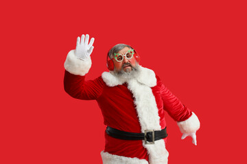 Funny Santa Claus in headphones listening to music and dancing on red background