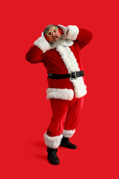 Funny Santa Claus in headphones listening to music and dancing on red background