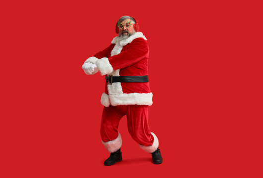 Funny Santa Claus in headphones listening to music and dancing on red background