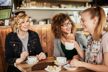 Three young women laughing sitting in cafe