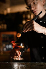 Female bartender holds a slice of orange peel with tweezers