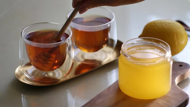 Putting golden honey into cup with hot tea with wooden dipper. 4K video