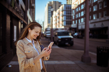 Young smiling woman with headphones using mobile phone in city