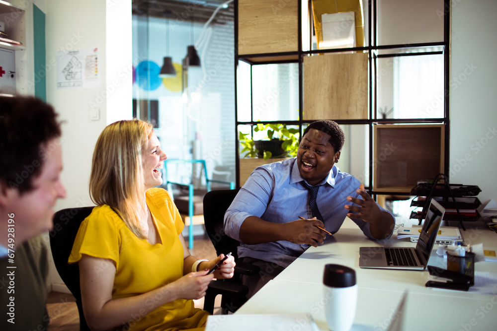 Wall mural young colleagues laughing during meeting in modern office