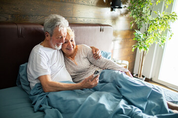 Senior couple using mobile phone together in bed at home