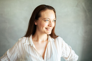 Portrait of a smiling beautiful young woman looking away with grey background