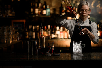 Female bartender pours an alcoholic drink from a geyser bottle into a jigger