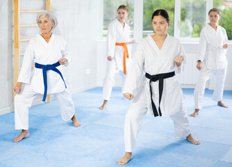 Experienced skilled young female karate sensei wearing white kimono adorned with black belt to prove mastery of martial arts techniques, leading group of women during kata training © JackF