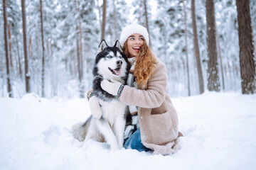 A cheerful husky dog walks with its owner in a snowy forest. A young woman with her pet on an adventure. Friendship concept, pets.
