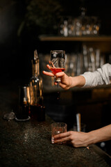 Female hands skillfully holds a small geyser bottle and pours a drink from it into a glass with ice
