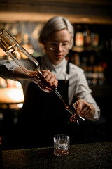 Female bartender prepares a cocktail by pre-pouring one of the ingredients into a jigger