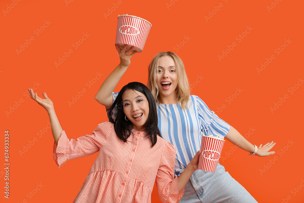 Poster beautiful young women with buckets of popcorn on orange background