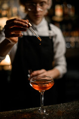 bartender adds a few drops of liquid to a ready-made cocktail in a cocktail glass with a pipette