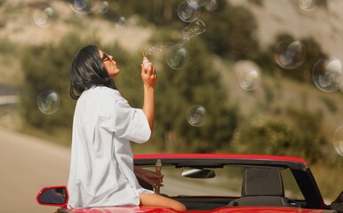 Fototapeta premium A beautiful woman with blowing bubbles in car