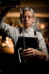 Serious female bartender pours a clear liquid from a shaker into a metal glass