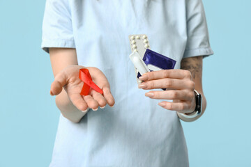 Beautiful young woman with contraceptive pills, red ribbon and condom on blue background. AID awareness concept