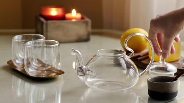Pouring dry tea leaves into glass teapot on table with cup, honey and lemon. 4k video