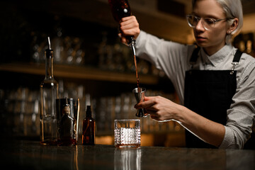 Female bartender fills a metal jigger from a geyser bottle with alcohol