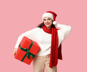 Beautiful young woman in Santa hat with Christmas gift on pink background