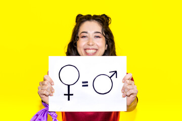 Young latina woman holding a sign claiming gender equality on yellow background. Concept of the...