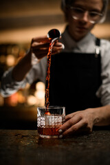Female bartender pouring an alcoholic drink into a glass for making a cocktail